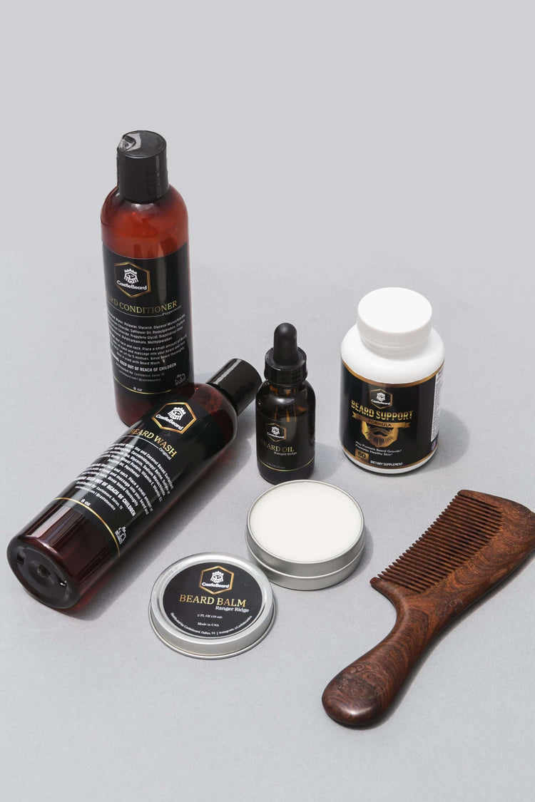 Full Beard Grooming Kit with beard wash, oil, balm, supplement, and wooden comb on a gray background.