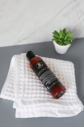Beard conditioner bottle on a textured white towel with a small green plant in the background.