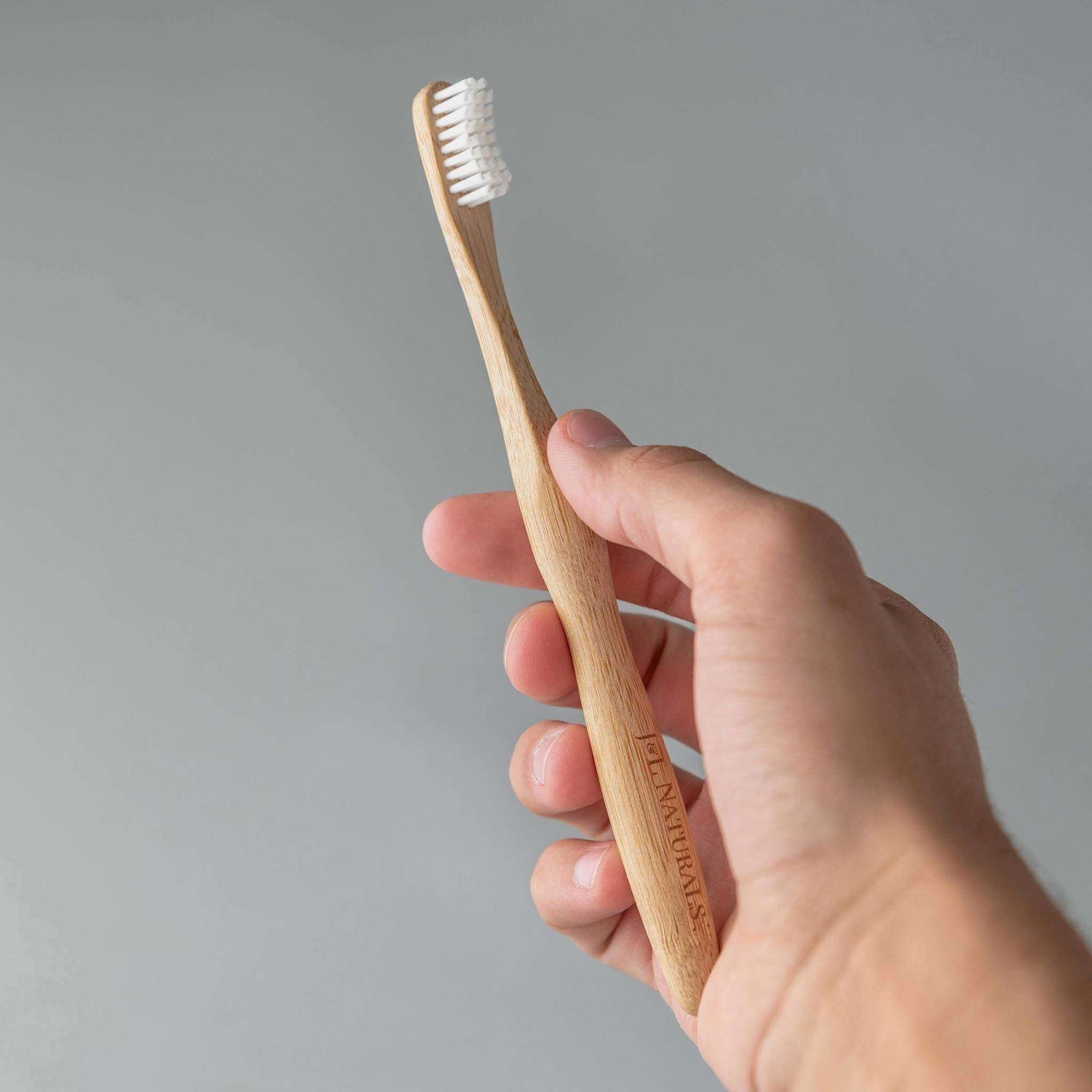 Bamboo toothbrush held in hand, featuring ergonomic design and eco-friendly materials in a modern style.