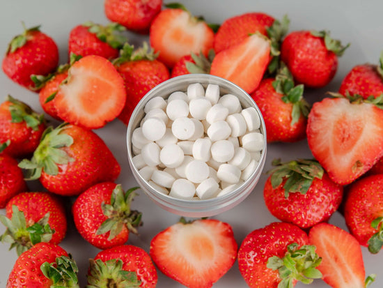 All Natural Toothpaste Tablets in a silver container surrounded by fresh strawberries, promoting dental hygiene.