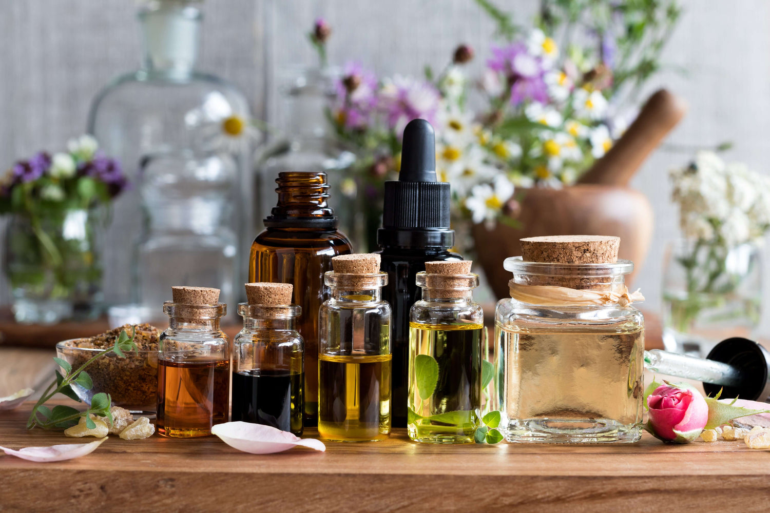 Collection of organic essential oils in various glass bottles with flowers in the background for herbal wellness.