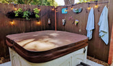 Cozy backyard with a hot tub covered, surrounded by plants and decorative items, twinkling lights, and hanging towels.