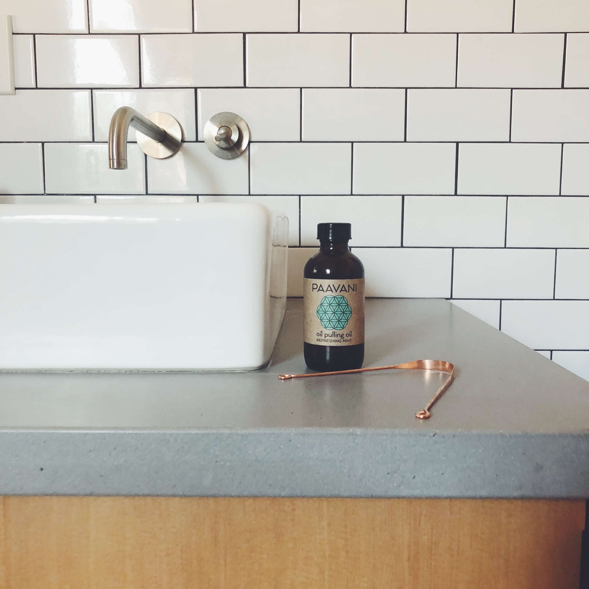 The Oral Care Ritual - Mint oil pulling bottle next to a tongue cleaner on a bathroom counter.