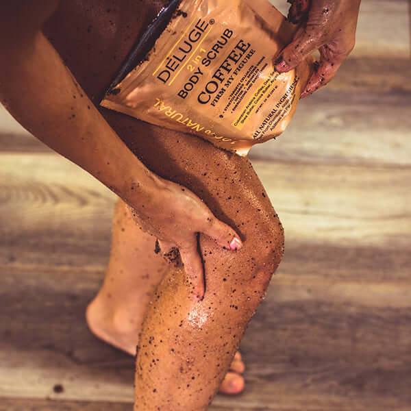 Person applying Deluge organic coffee body scrub on leg for exfoliation and hydration.