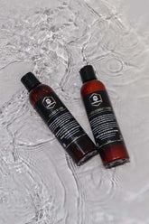 Beard wash and conditioner set bottles on wet surface, designed for cleaning and conditioning beards without stripping oils.