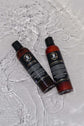 Beard wash and conditioner set bottles on wet surface, designed for cleaning and conditioning beards without stripping oils.
