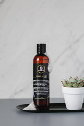 Beard wash bottle with foam next to a succulent on a modern tray, designed for men’s beard care.