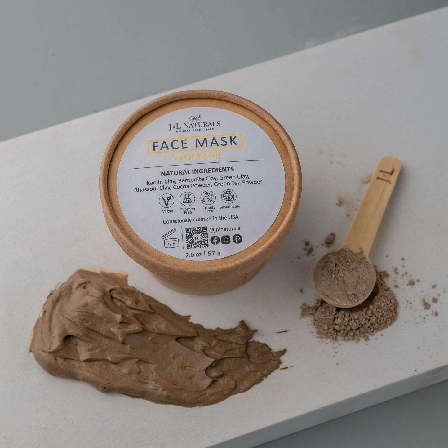 Natural clay face mask with ingredients, scoop, and application on a surface.