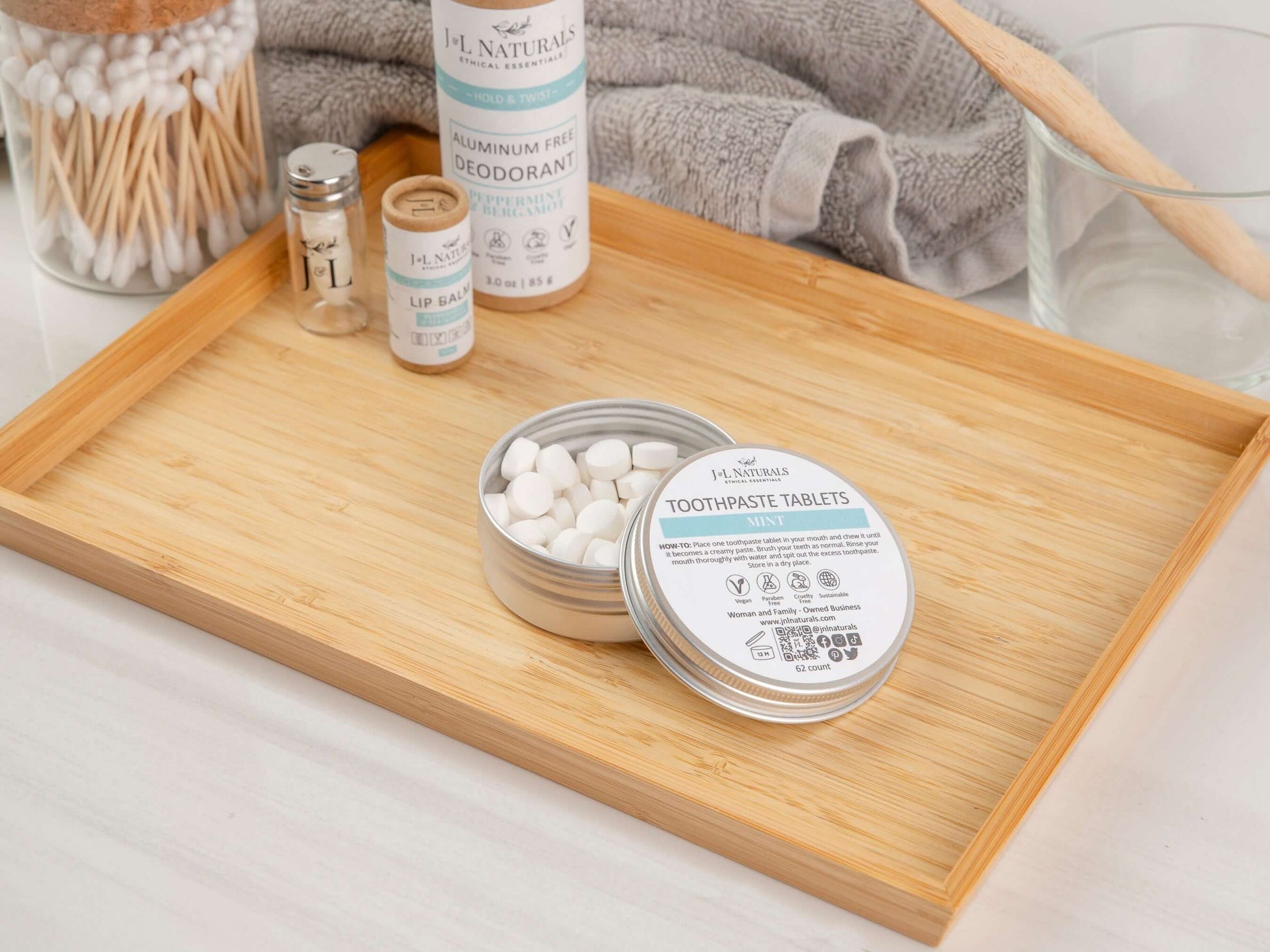 Eco-friendly toothpaste tablets in a tin on a bamboo tray with dental hygiene products.