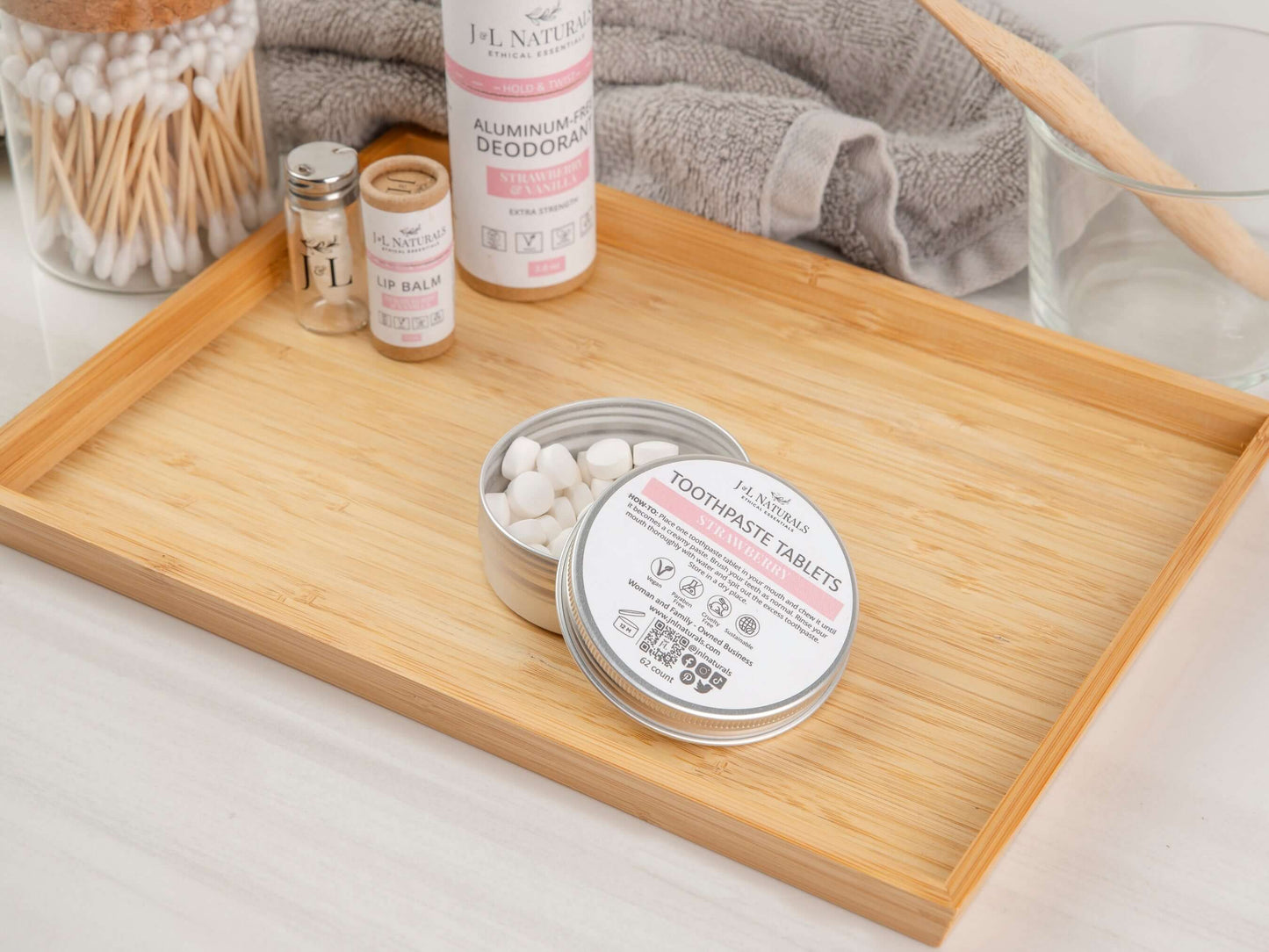 Eco-friendly toothpaste tablets in a tin on a bamboo tray with personal care items.