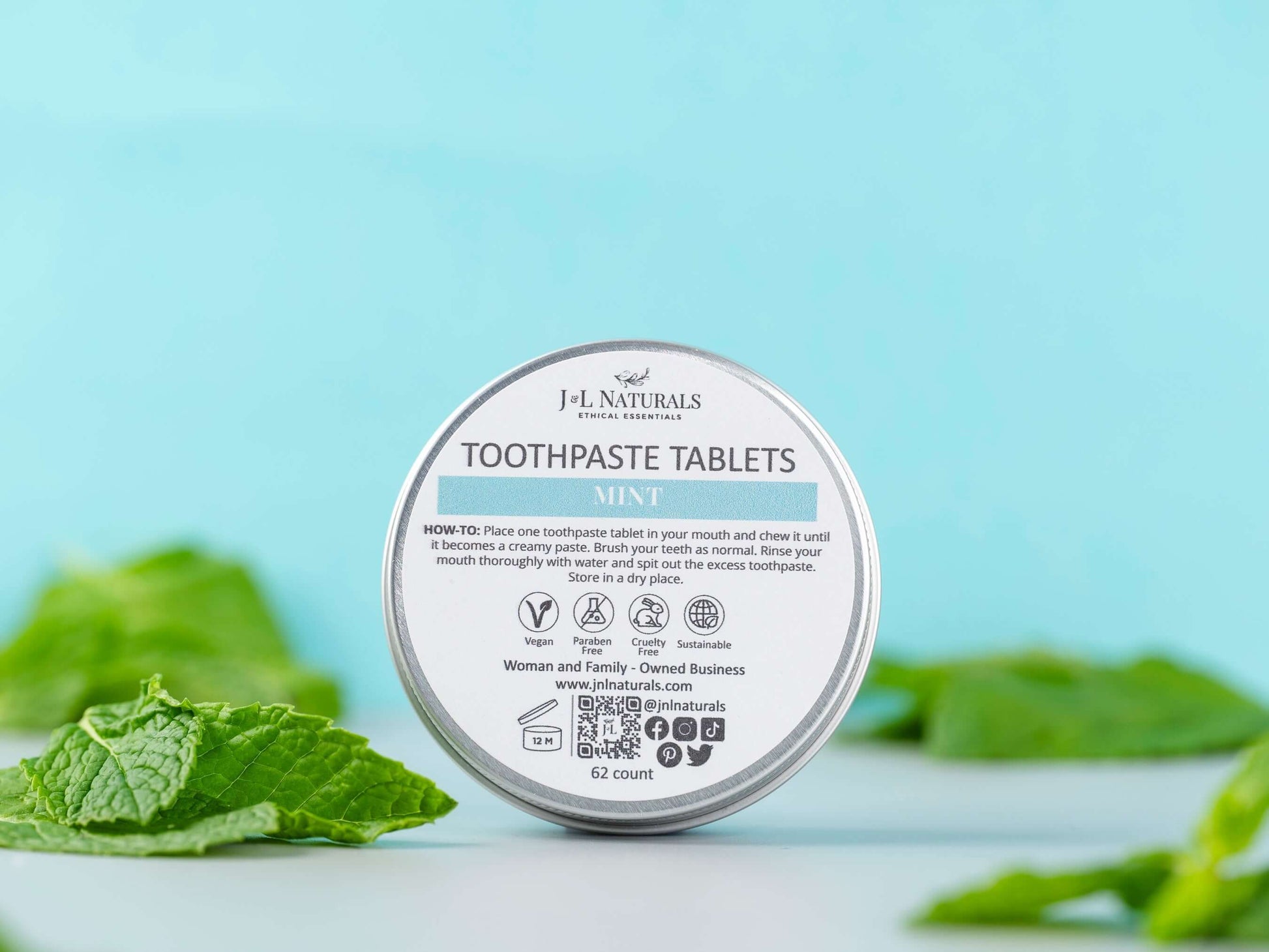 Eco-friendly mint toothpaste tablets packaging on a blue background surrounded by fresh mint leaves.