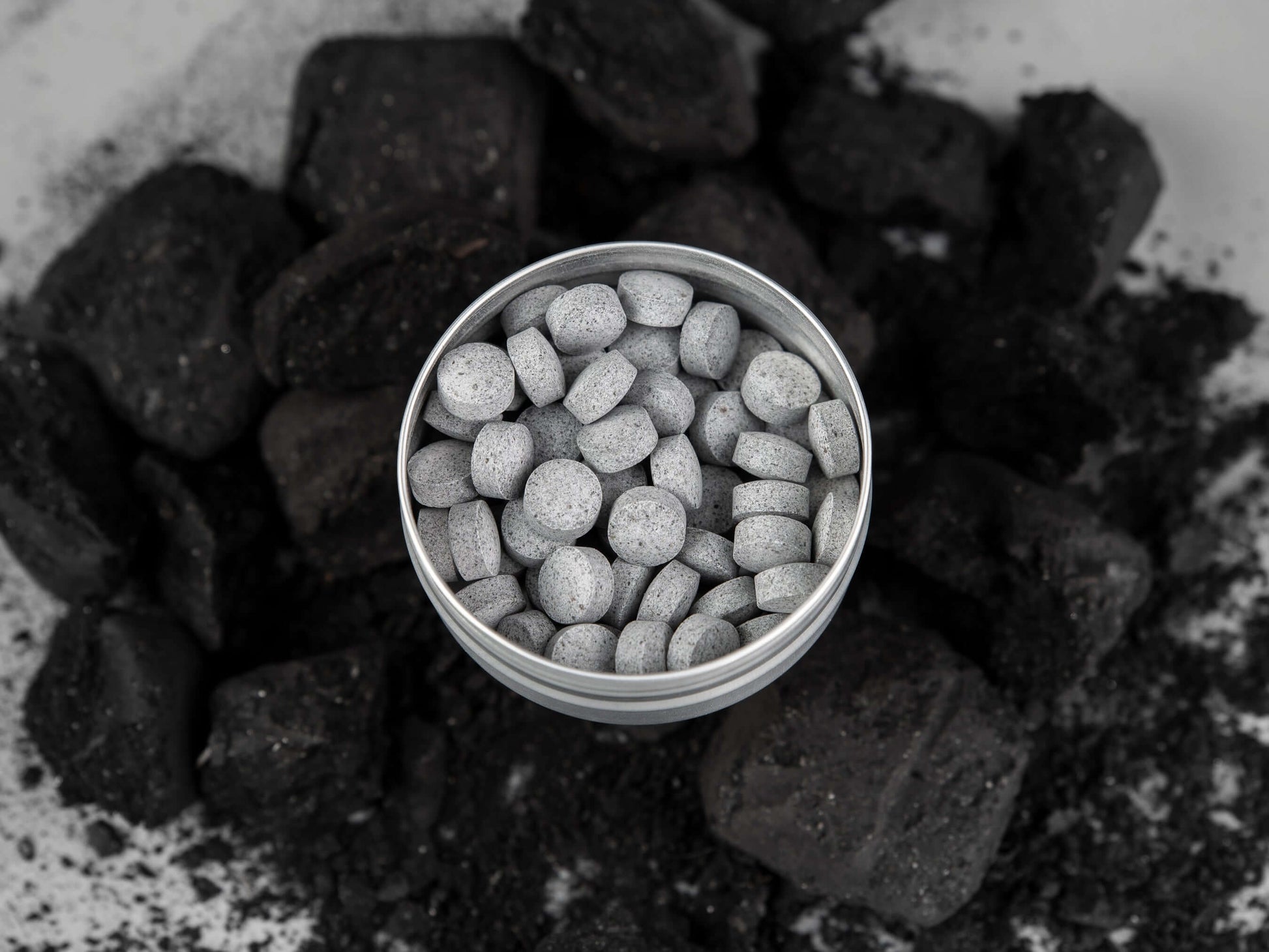 All-natural toothpaste tablets in a tin surrounded by charcoal pieces for eco-friendly dental hygiene.