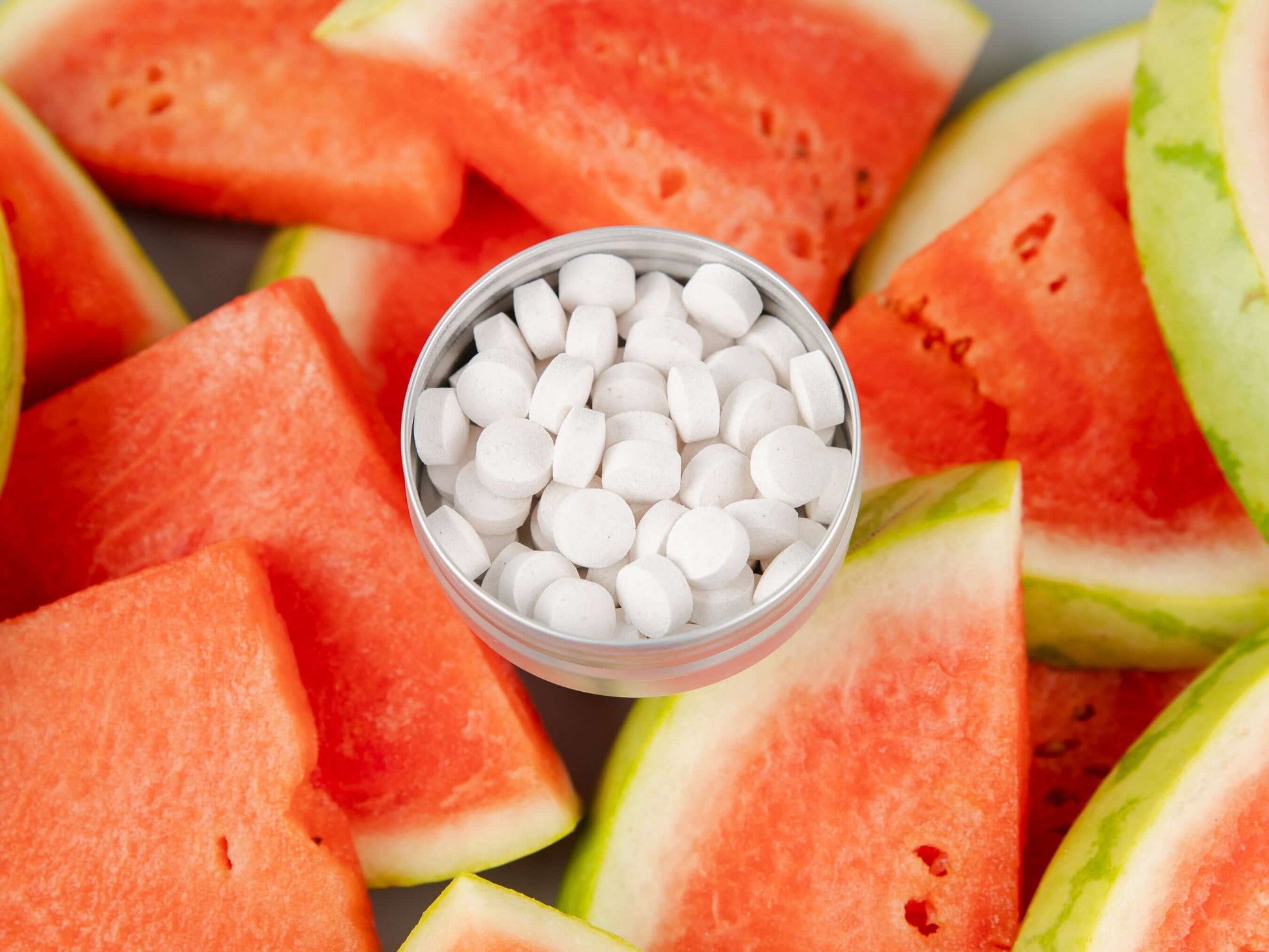 Toothpaste tablets in a round container on a backdrop of fresh watermelon slices, promoting eco-friendly dental care.