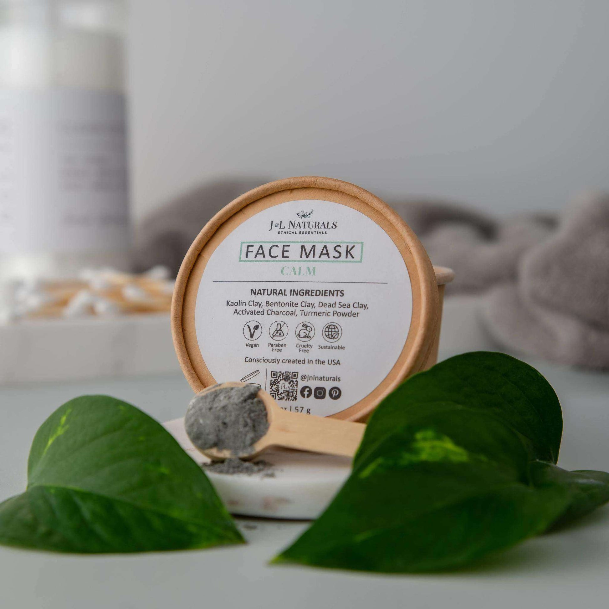 Calm face mask with natural ingredients in eco-friendly packaging surrounded by green leaves.