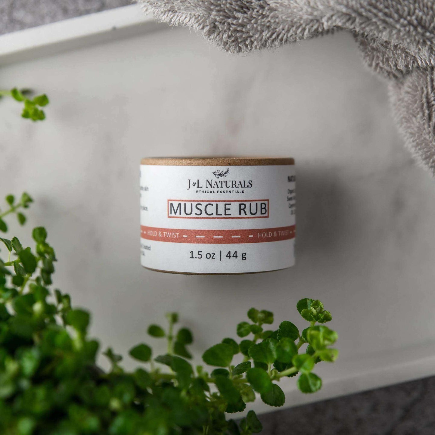 Muscle Rub by J.L. Naturals in a 1.5 oz container, surrounded by greenery for soothing muscle relief.