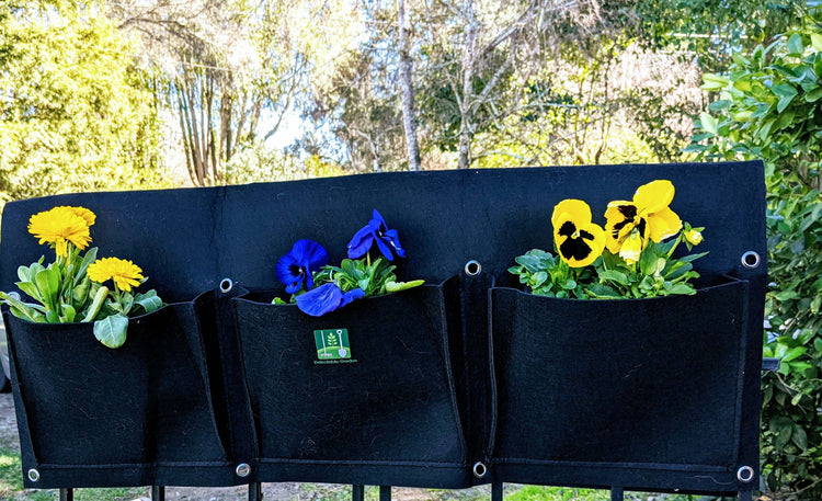 Colorful flowers in a cloth 6 pocket saddlebag hanging vertical garden planter on a fence.