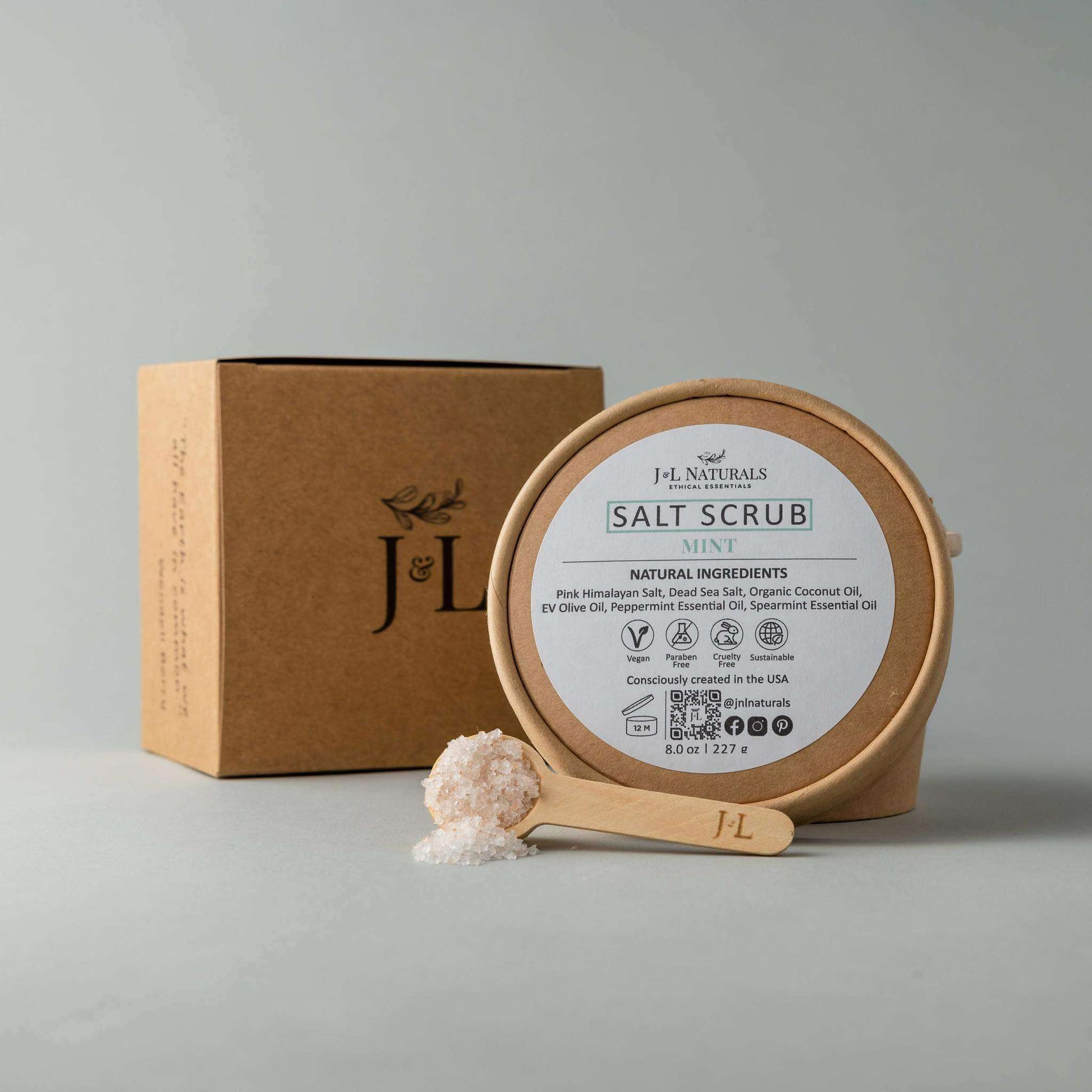 Salt scrub with mint in a wooden container, accompanied by a scoop and packaging, showcasing natural exfoliating ingredients.