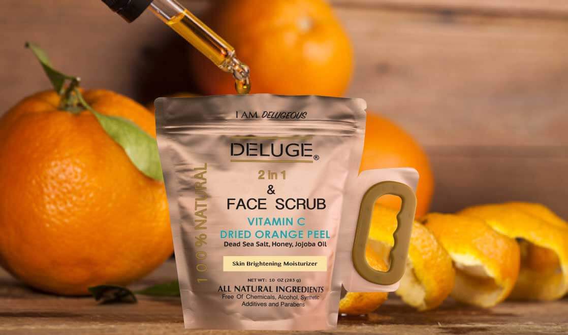 Deluge Vitamin C scrub with dried orange peel, honey, and jojoba oil beside fresh oranges on wooden surface.