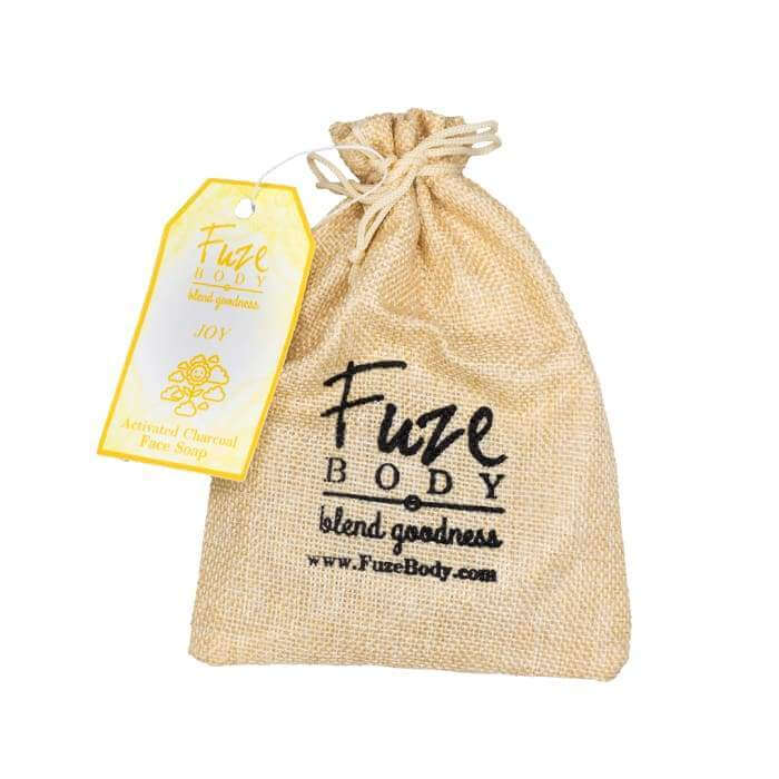 Joy Activated Charcoal Facial Soap in a natural burlap bag with tag featuring product details and brand name.