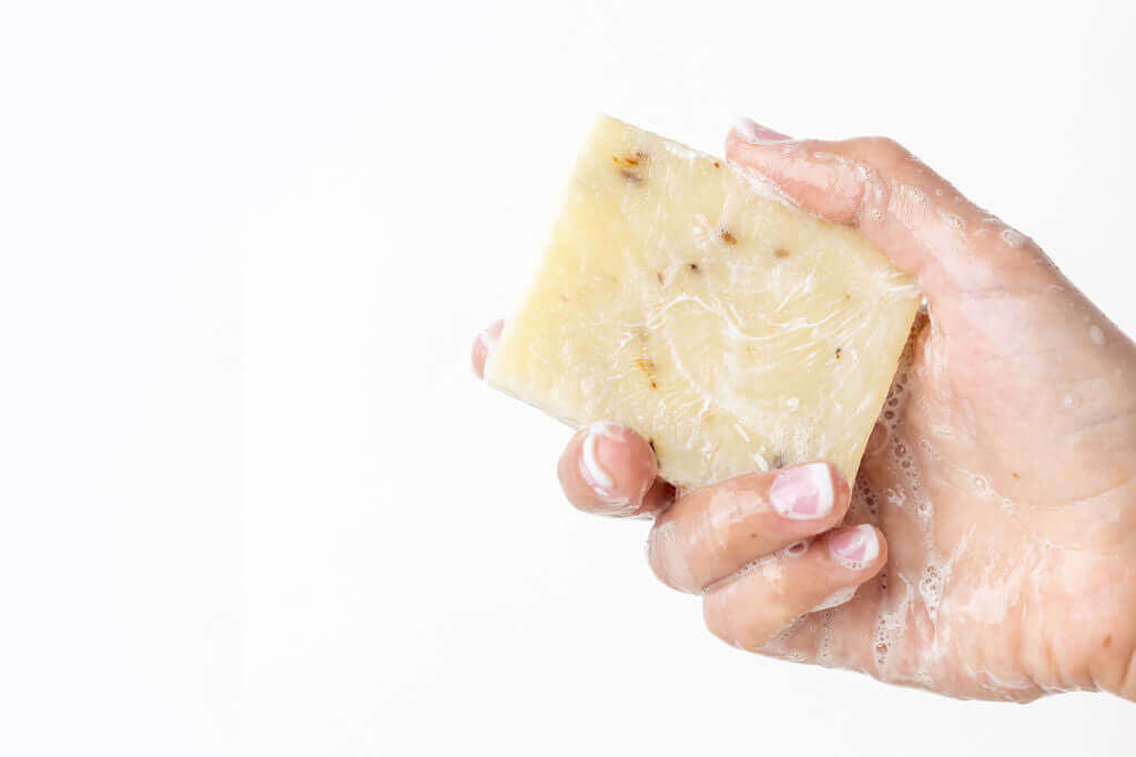 Hand holding a natural citrus soap bar with bubbles for a refreshing bath experience.