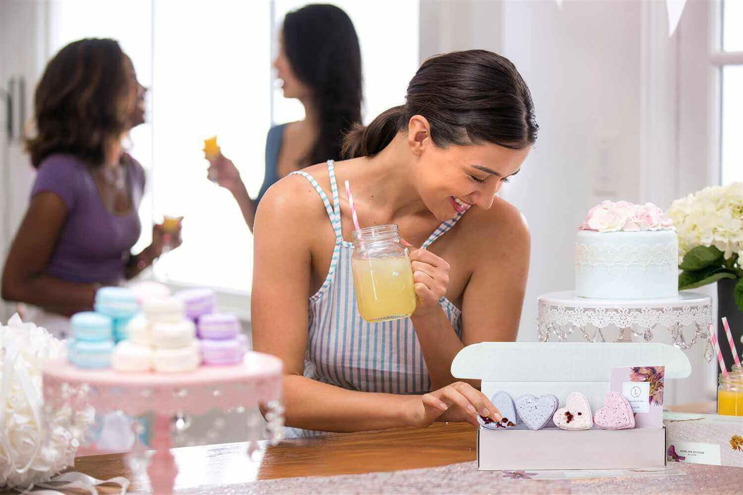 Woman enjoying a refreshing drink while unboxing heart-shaped shower steamers at a celebration with friends.