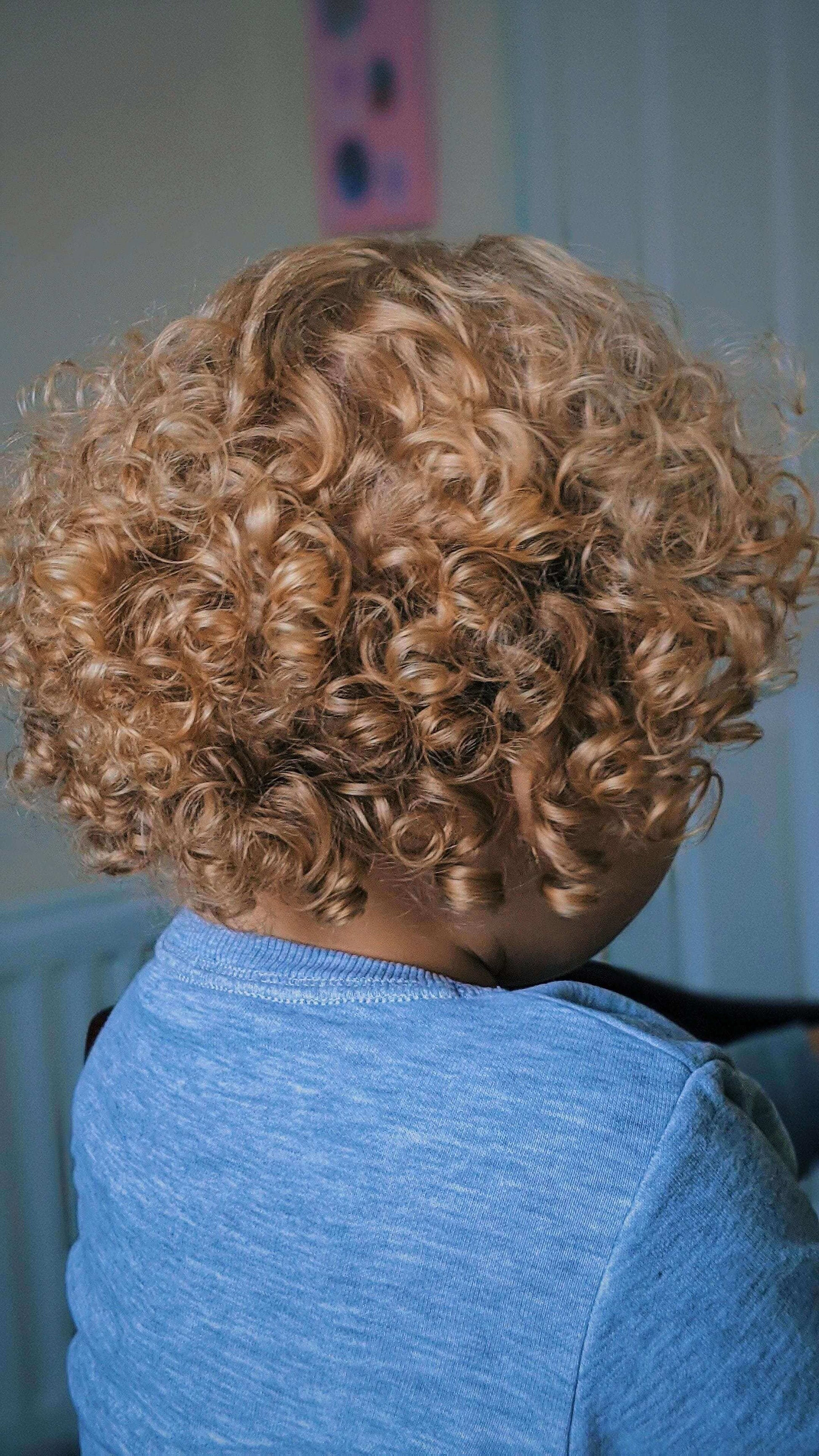 Back view of a child with beautiful, bouncy, blonde curls, showcasing healthy and vibrant natural hair.