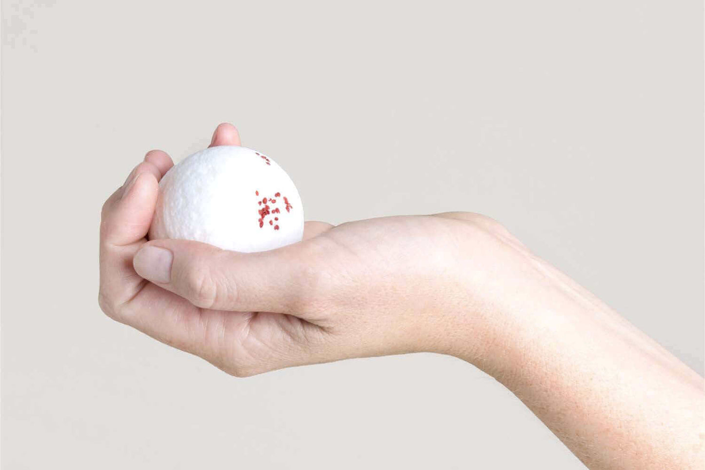 Person holding a white golf ball with red markings in hand against a neutral background.