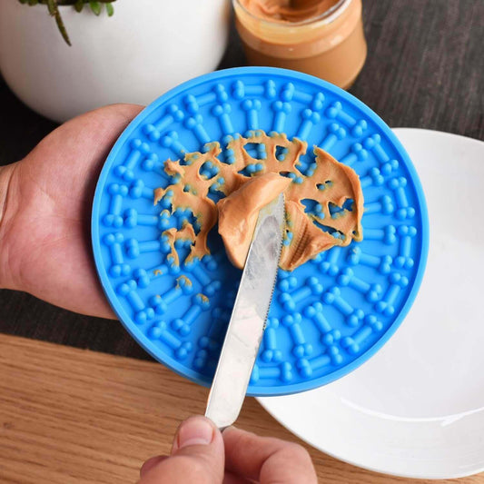 Person spreading peanut butter on a blue dog distraction lick mat with suction cups for bath time engagement.